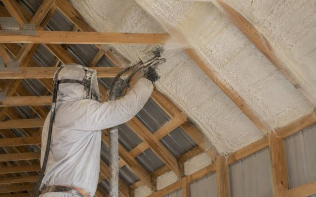 Installer spraying foam between rafters under a metal roof in Cambridge